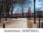 A gorgeous winter landscape at the Marietta Square with red brick footpath, a water fountain, bare trees, pink trees, and lush green plants with a clear blue sky in Marietta Georgia USA