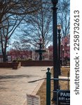 A gorgeous winter landscape at the Marietta Square with red brick footpath, a water fountain, bare trees, pink trees, and lush green plants with a clear blue sky in Marietta Georgia USA