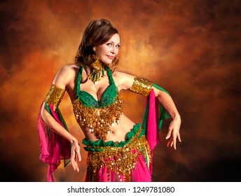 Gorgeous woman bellydancer dancing in traditional bellydance costume over colored studio background.