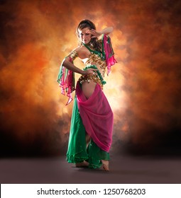 Gorgeous woman bellydancer dancing in traditional bellydance costume over colored studio background.