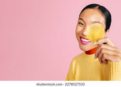 Gorgeous woman with a bold two tone lipstick smiles at the camera as she holds up a yellow cap from a cosmetic product, highlighting her love of vibrant makeup and beauty products. - Shutterstock ID 2278527533