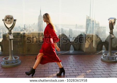 Gorgeous woman in red dress and leather boots walks on the roof of Rockafeller Center in New York
