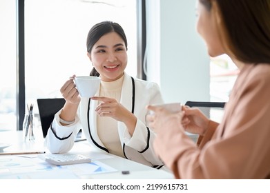 Gorgeous Young Asian Female Boss Or Marketing Manager Having A Good Conversation With Her Assistant During The Coffee Break In The Office.