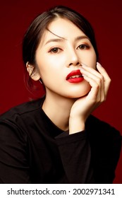 Gorgeous Young Asian Female Close Up Face With Perfect Make-up And Red Lips. Beautiful Woman In Black Sweater Look Confidence And Chraming. Isolated On Red Background.