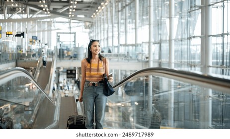 A gorgeous young Asian female tourist passenger is on an airport escalator, carrying her luggage, going to the airport check-in counter, traveling by plane. people and transportation concepts - Powered by Shutterstock