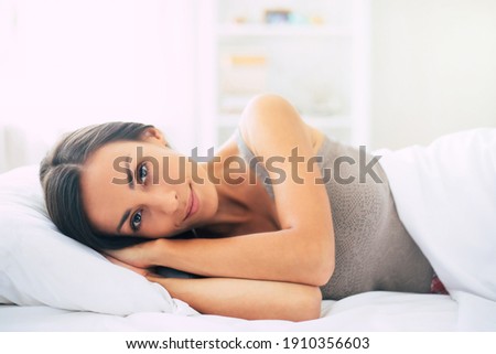 Gorgeous young brunette woman lying in big white bed during relaxing at home