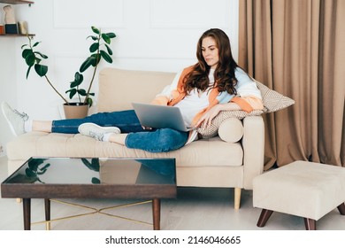 Gorgeous Young Business Woman Lying On A Sofa Works Remotely On A Laptop Computer.