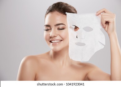 Gorgeous Young Girl  With Naked Shoulders Posing At Grey Background With Facial Mask, Skin Care Concept, Beauty Photo, Skin Treatment, Hydrating Skin Mask, Smiling.