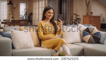Gorgeous Young Indian Woman Making a Video Call on Her Smartphone at Home, Sharing Laughs and Gossip with Girfriends. Stunning Girl with Magnificent Smile talks to Her Boyfriend Online.