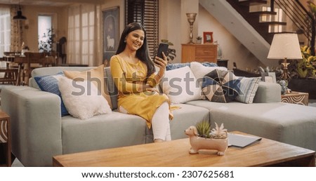 Gorgeous Young Indian Woman Making a Video Call on Her Smartphone at Home, Sharing Laughs and Gossip with Girfriends. Stunning Girl with Magnificent Smile talks to Her Boyfriend Online. Medium Shot