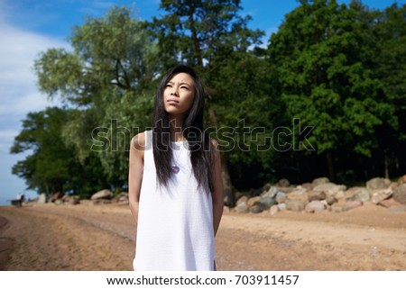 Gorgeous young Japanese woman spending holidays by the ocean, walking along shore, having thoughtful serious look, breathing fresh sea air. Pensive Chinese student girl enjoying summer vacations