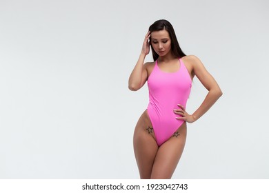Gorgeous young slim brunette in stylish pink bikini with sunglasses in hand looking at camera on white background