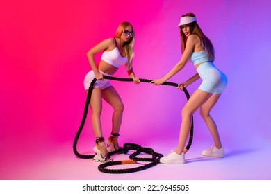 Gorgeous Young Sportswomen Pulling Battle Rope Against Bright Gradient Background