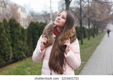 Gorgeous young woman with beautiful eyes and brunette, with natural make-up. Attractive young lady on city street, turns to camera and gives a lovely playful smile. fur collar