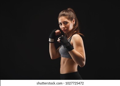 Gorgeous young woman with boxing bandage, standing in the defending position, ready to fight, copy space. Studio shot on black background, low key. Kickboxing and fight sport concept - Powered by Shutterstock