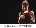 Gorgeous young woman with boxing gloves, standing in the defending position, ready to fight, copy space. Studio shot on black background, low key. Kickboxing and fight sport concept