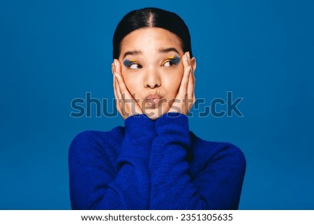 Gorgeous young woman embracing her face and looking away while wearing makeup. Young gen z woman enjoying herself in graphic eyeliner and lip gloss.