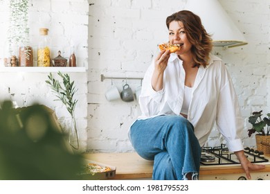 Gorgeous Young Woman Plus Size Body Positive In Blue Jeans And White Shirt Eating Pizza In Home Kitchen