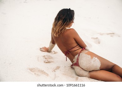 A Gorgeous Young Woman In A Red Bikini With A Sexy Ass Lies On The Beach With White Sand. Summer Vacation Girl On The Island. Model Tans And Poses Near The Ocean.