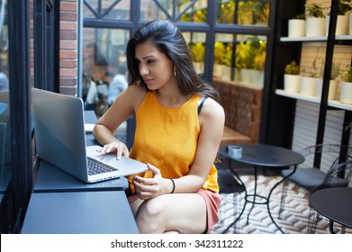 Gorgeous young woman sitting with open laptop computer in modern coffee shop interior, female freelancer using net-book for her distance work, student girl learning via portable gadget device