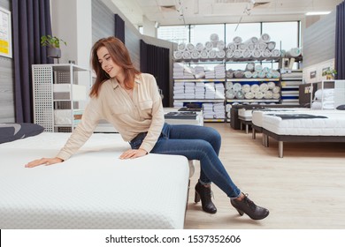 Gorgeous Young Woman Smiling, Examining Orthopedic Mattress On Sale At Furniture Store, Copy Space