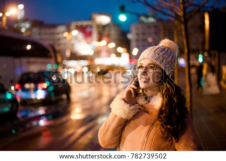 Gorgeous young woman talking on phone in city street, traffic lights on background.