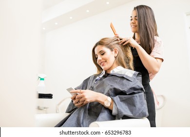 Gorgeous young woman using her smartphone and texting during her visit to a hair salon - Powered by Shutterstock