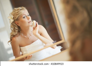 Gorgerous Bride Standing In Front Of Mirror And Fixing Her Hair And Make Up. Putting Earings, Powdering And Smilling. Wedding Preparation In Hotel Room. 