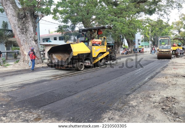 Gorontalo, October 5, 2022 : Asphalt paver machine\
and truck. Road construction crew apply the first layer of asphalt.\
Hot mix asphalt paving and road work - Flatten out the hot asphalt\
road with road
