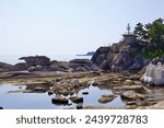 Goseong County, South Korea - July 30, 2019: Coastal rocks at Cheonjin Beach trap placid waters from the East Sea, with a retired military lookout post perched atop a rocky outcrop.