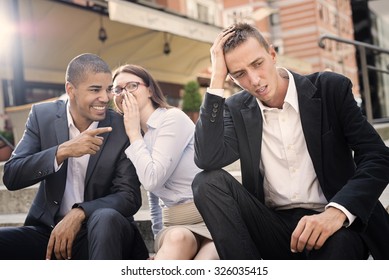 Gossip people in front of their office sitting on stairs,depressed businessman portrait and gossip out of focus in background.