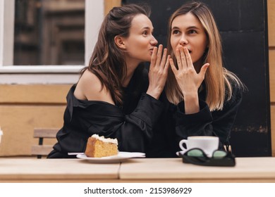 Gossiping. Two beautiful young women gossiping telling something on ear while sitting in the cafe. Communication and friendship concept. Young woman telling her friend some secrets.