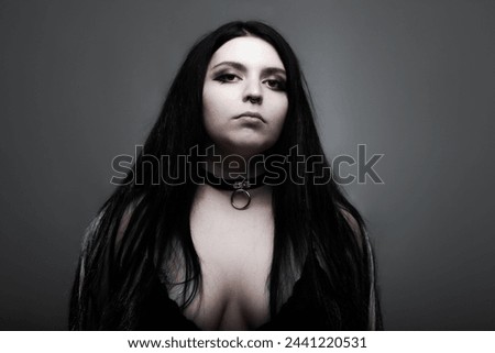 Goth girl with white eyes and long dark hair against dark gray background.