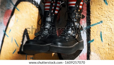Goth teenager girl slide with rough boots striped stockings sits on ornate wall of an abandoned building. Alternative in youth. An alternative in youth. Hipster, freak, emo, grunge. Copy 