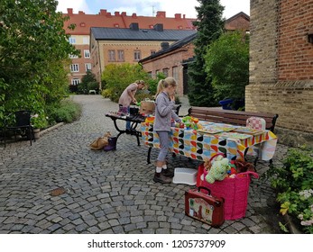 Gothenburg,Sweden-Circa September 2018: Swedish Kid Sets Up Her Selling Knickknacks,dolls And Secondhand Toys On Table In The Garden Beside Her Mom’s Table For Garage Sales.