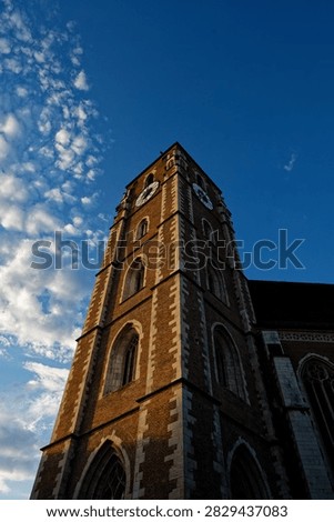 Gothic brick clock tower under a deep blue sky with wispy clouds during golden hour.