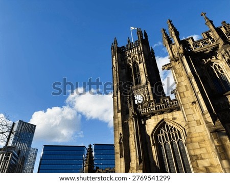 Gothic cathedral tower and clock face beside contemporary glass offices under vibrant blue sky in Manchester