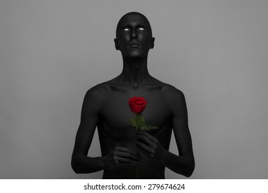 Gothic And Halloween Theme: A Man With Black Skin Holding A Red Rose, Black Death Isolated On A Gray Background In Studio