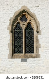 Gothic leaded glass window on the outside of a church set within a white washed stone wall.