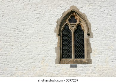 Gothic leaded glass window set within a white washed church stone wall.