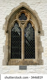 Gothic leaded glass window set within a lime washed stone church wall.