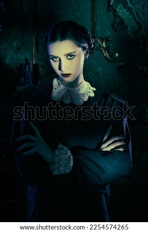 Gothic portrait of an attractive brunette girl with black eyes in a strict black dress with a white collar, standing in a gloomy old mansion at night. The Addams Family. Gothic novel, mysticism.