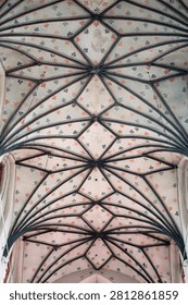 Gothic rib vault ceiling architecture inside a historic church, featuring pale stone ribs and plaster panels painted with repeating green and orange floral cross patterns.