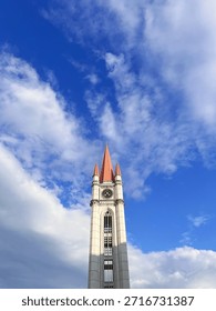  Gothic style clock tower with red spires under a bright blue sky and white clouds, architectural landmark exterior.