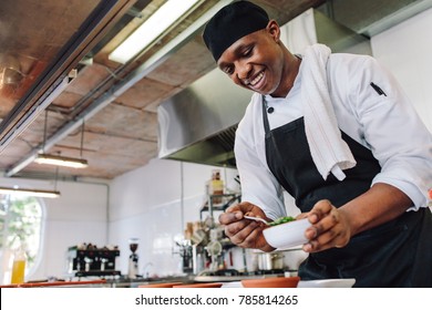 Gourmet chef in uniform cooking in a commercial kitchen. Happy male cook wearing apron standing by kitchen counter preparing food.
