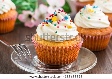 Gourmet cupcakes with white buttercream frosting and sprinkles on wooden background