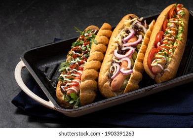 Gourmet dirty hot dog sandwich with various garnish on black stone background. Healthy option of fast food.