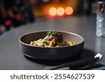 Gourmet dish in focus, featuring grilled meat with garnish in a ceramic bowl. Close-up composition with shallow depth of field, soft bokeh of candlelit background, and wine glass adding elegance.