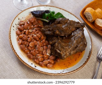Gourmet dish - pork tenderloin fried to golden crust with side dish of tender and soft stewed beans in their own juice. Dinner plate is decorated with parsley, spinach, basil leaves - Shutterstock ID 2396292779