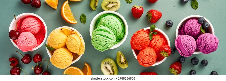 Gourmet flavours of Italian ice cream served in individual ice cream paper cups on blue background. Strawberry sorbet, blueberry ice cream with orange sorbet and kiwi ice cream decoration with mint
